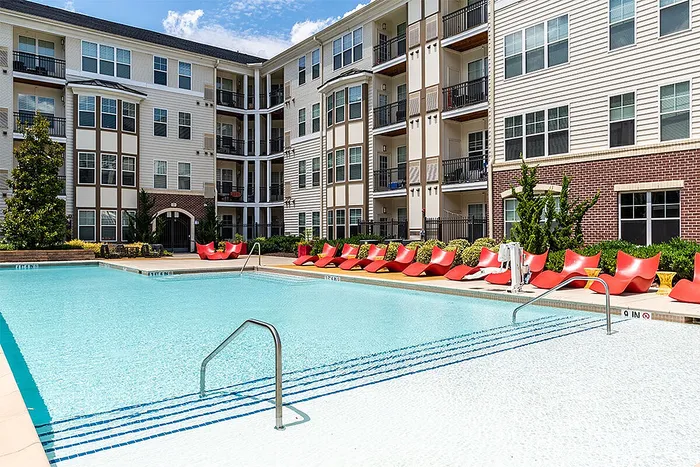 Modern apartment complex with a refreshing outdoor pool and eye-catching red lounge chairs, perfect for relaxation and leisure.
