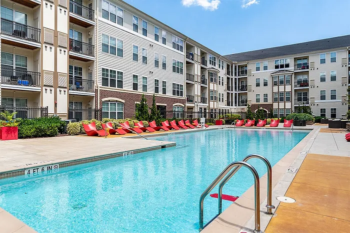 Modern apartment complex featuring a sparkling outdoor pool with stylish red lounge chairs, ideal for relaxation and leisure.