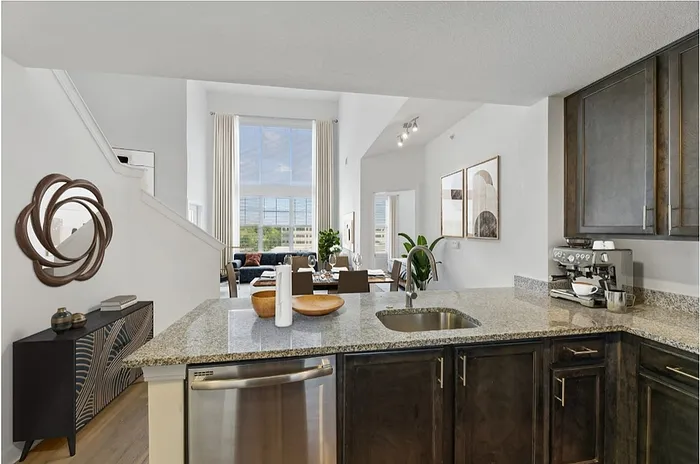 Elegant open-plan kitchen with granite countertops, leading to a bright living area featuring large windows and modern decor.