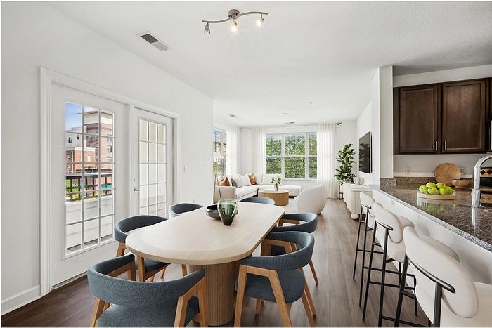 Bright and modern living space with an open-concept dining and kitchen area, featuring sleek furnishings, large windows, and elegant decor.