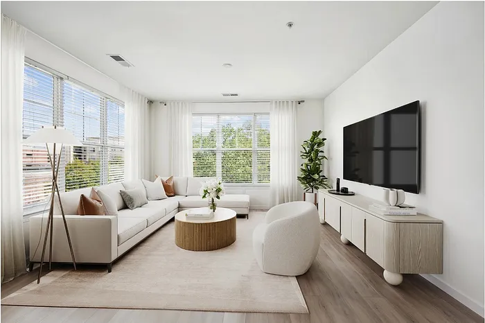 Bright and modern living room with a cozy L-shaped sofa, elegant decor, and a large flat-screen TV, offering a serene and inviting atmosphere.