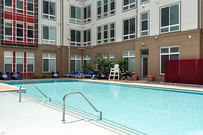 Modern apartment complex featuring a sparkling swimming pool with chic lounge chairs, surrounded by contemporary architecture and lush greenery.