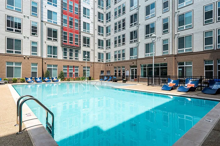Modern apartment complex with a stunning outdoor pool, sleek blue lounge chairs, and stylish architecture.