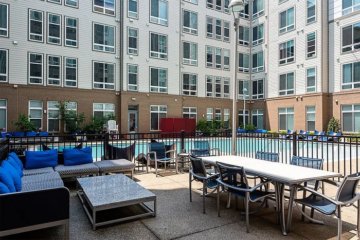 Modern apartment courtyard with inviting blue seating, a stylish patio table, and a stunning pool backdrop.