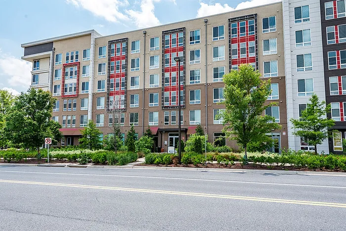 Modern apartment building with eye-catching red accents, featuring lush greenery and large windows for natural lighting.