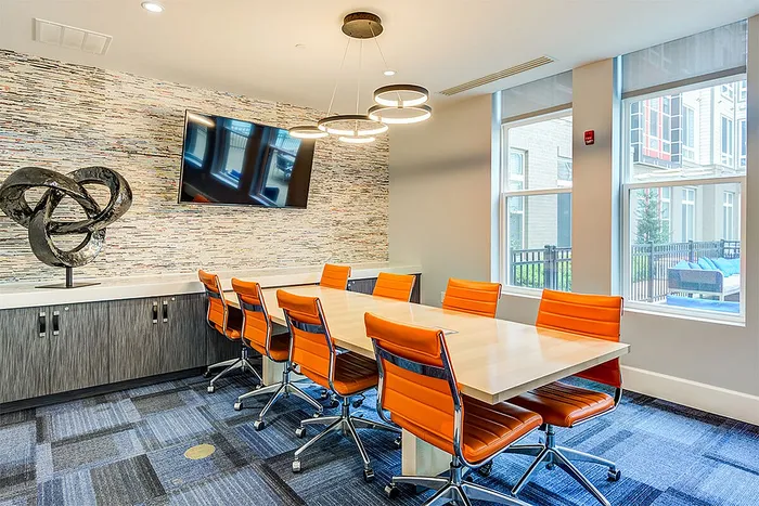 Modern conference room featuring vibrant orange chairs, a sleek table, unique abstract wall art, and a large wall-mounted screen.
