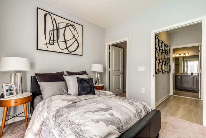 Elegant bedroom featuring a cozy bed, stylish abstract artwork, and a glimpse of an attached modern bathroom.
