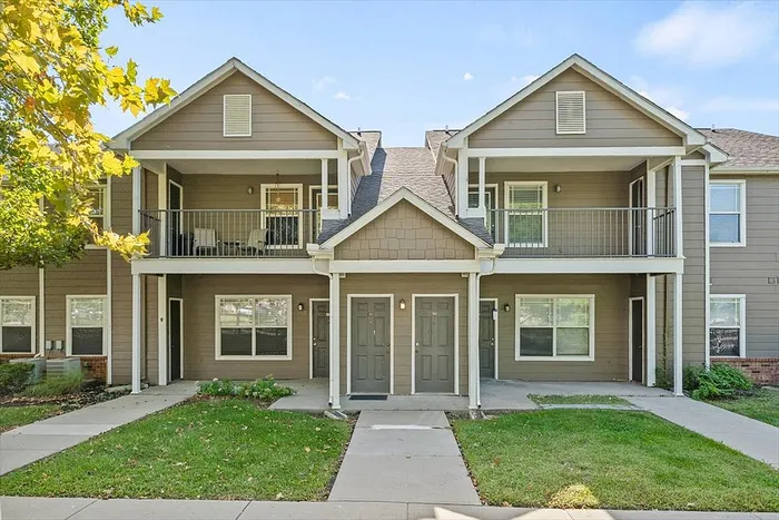 Charming two-story apartment with private balconies, modern exterior, and lush landscaping, perfect for comfortable living.