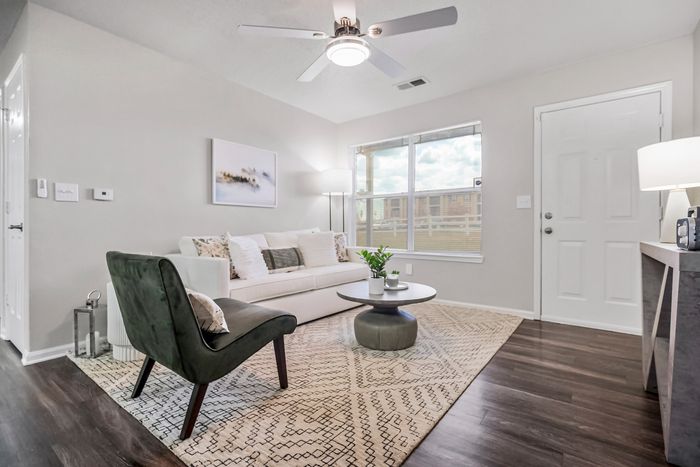 Bright and inviting living room with modern decor, featuring a cozy white sofa, elegant chair, and stylish round coffee table on a patterned rug.