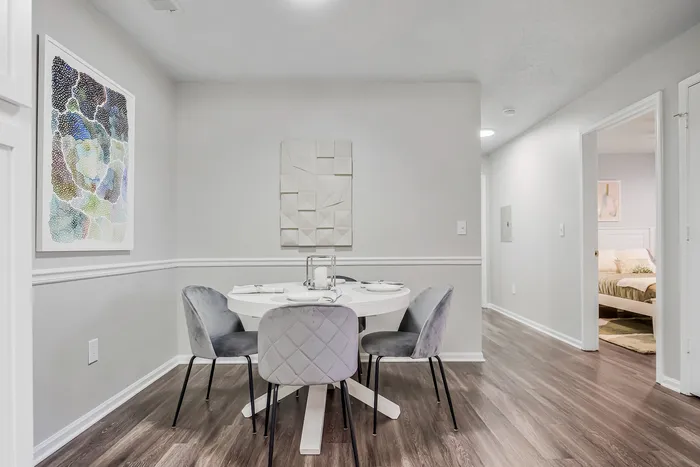 Chic dining area with modern art, round white table, and upholstered chairs on elegant hardwood floors.
