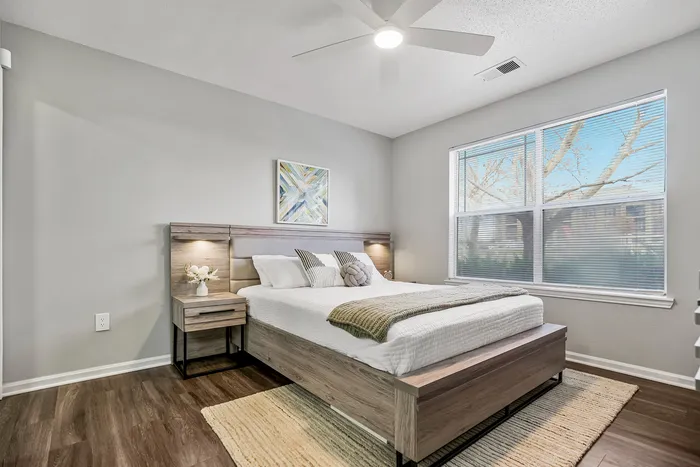 Elegant bedroom featuring a modern wooden bed, cozy textiles, and soft natural light from a large window.