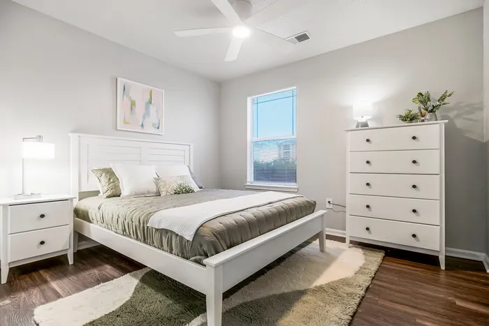 Bright and inviting bedroom featuring modern white furniture, cozy bedding, and warm wooden floors.