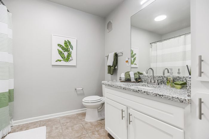 Bright and modern bathroom featuring chic granite countertops, sleek white cabinetry, and stylish green accents.