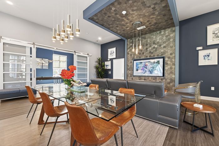 Modern apartment lounge with sleek glass dining table, leather chairs, and stylish lighting fixtures in a vibrant, open-concept setting.