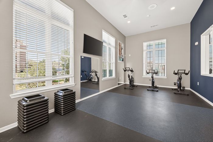 Bright and modern fitness room with large windows, featuring exercise bikes and sleek gym equipment for a refreshing workout experience.