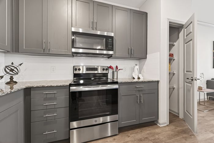 Modern kitchen with sleek gray cabinets, stainless steel appliances, and granite countertops, seamlessly connecting to an inviting living space.