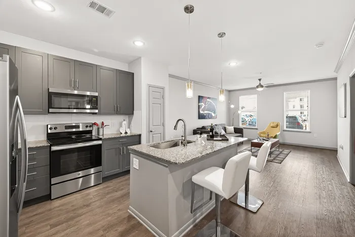Modern open-concept kitchen and living room with sleek granite countertops, elegant pendant lighting, and stylish decor in a cozy apartment setting.