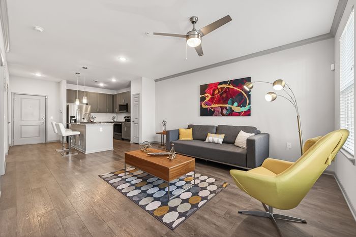 Contemporary living space featuring modern kitchen, elegant gray sofa, vibrant artwork, and stylish yellow accent chair.