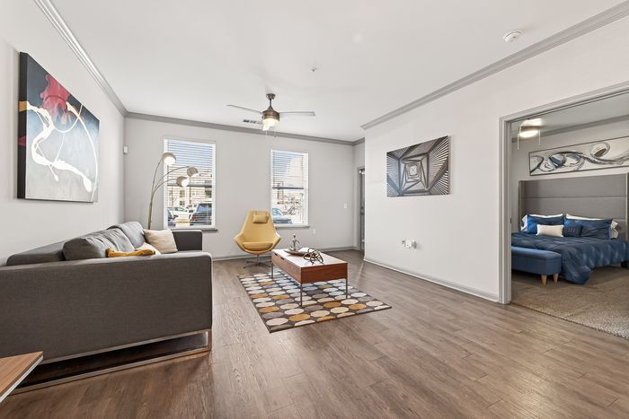 Modern living room with stylish decor, wood flooring, and a comfortable seating area, adjacent to a cozy bedroom with elegant bedding.