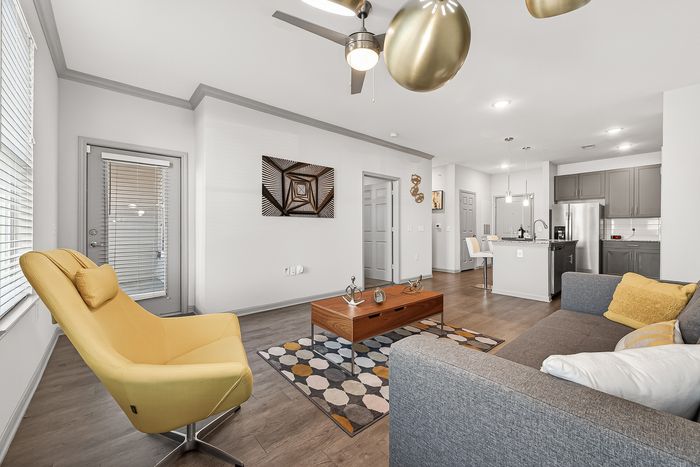 Modern open-concept living space with stylish gray couch, vibrant yellow chair, and contemporary kitchen design.