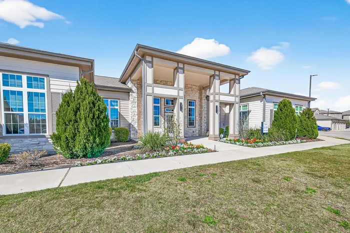 Charming suburban home exterior with elegant stone facade, large windows, and manicured landscaping under a clear blue sky.