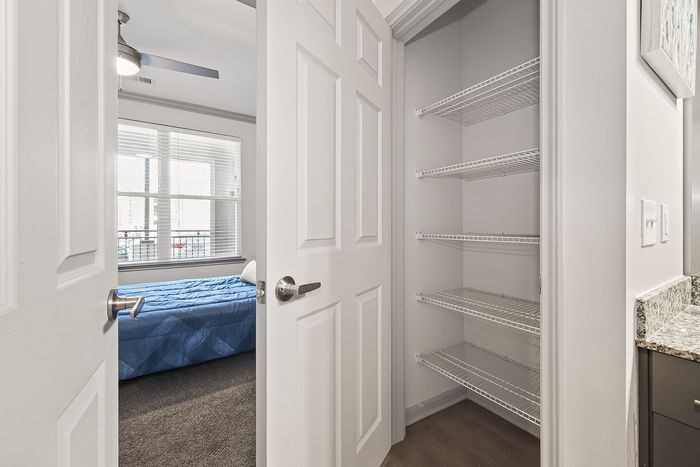 Bright and inviting bedroom with modern decor, featuring a cozy bed next to a large window for natural light, and a spacious closet with ample shelving for storage.