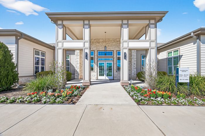 Elegant apartment entrance with a grand, covered walkway and vibrant flowerbed, showcasing modern architectural design.