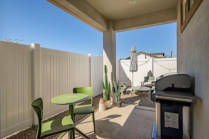 Charming patio with vibrant green furniture, a modern grill, and sleek potted plants against a sunny backdrop.