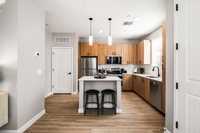Modern kitchen with sleek wooden cabinetry, stainless steel appliances, a stylish island with pendant lighting, and two cozy stools.