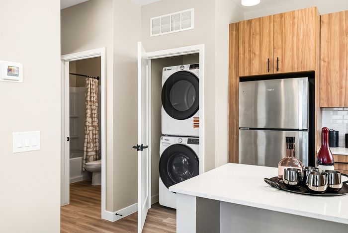 Modern apartment kitchen with stacked washer and dryer, elegant wooden cabinets, and a stainless steel refrigerator, showcasing convenience and style.