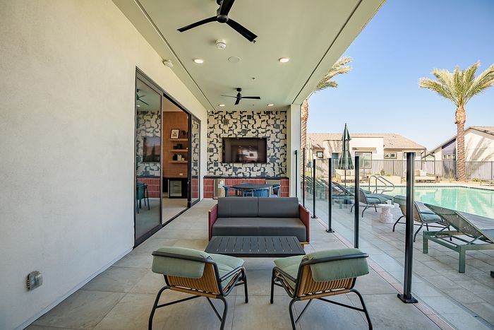 Luxurious modern patio with comfortable seating, poolside lounge chairs, and a stunning view of the pool surrounded by palm trees, perfect for relaxation and entertaining.