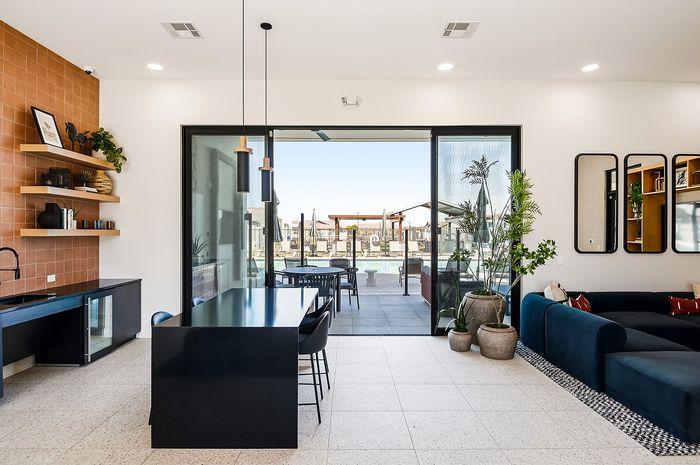 Modern open-concept living space with a stylish kitchen, elegant black dining table, and cozy living room leading to a serene poolside patio.