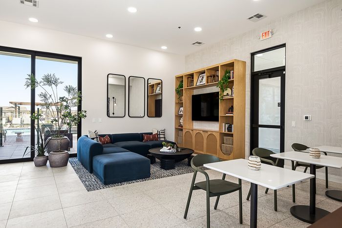 Modern lounge area with sleek blue sectional, stylish open shelving, and vibrant natural light from large windows overlooking a pool.