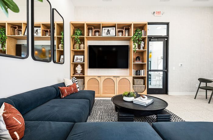Modern living room with stylish shelving, a large flat-screen TV, elegant mirrors, and a plush navy sectional sofa accented with decorative pillows.