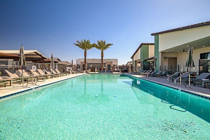 Luxurious apartment complex boasting a sparkling swimming pool with inviting lounge chairs and tropical palm trees, perfect for relaxation.