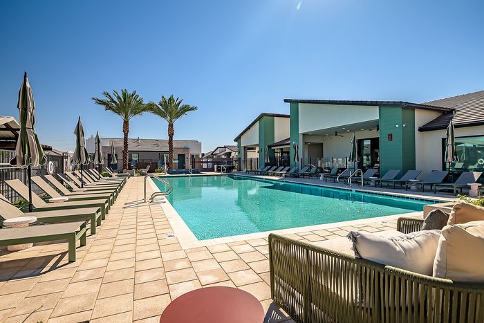 Luxurious apartment complex showcasing a pristine outdoor pool, surrounded by elegant lounge chairs and shaded umbrellas, framed by majestic palm trees and modern architecture.