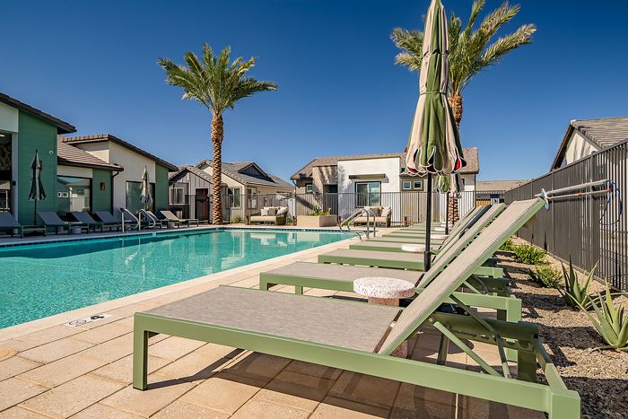 Luxurious apartment complex poolside oasis with sleek sun loungers, vibrant palm trees, and modern architecture under a clear blue sky.