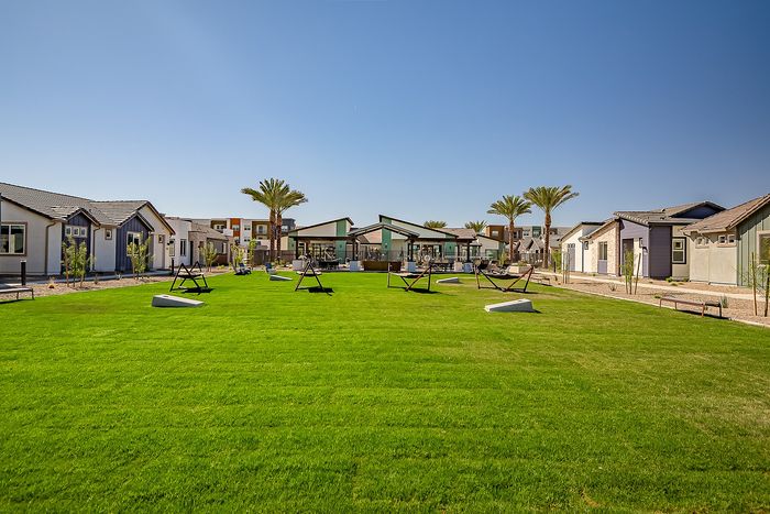 Inviting modern community space with lush green lawns, stylish patio seating, and charming bungalows under a clear blue sky.