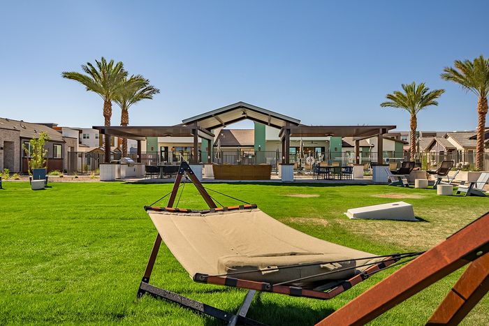 Inviting outdoor living area featuring lush green lawn, a relaxing hammock, modern seating area, and towering palm trees under a clear blue sky.