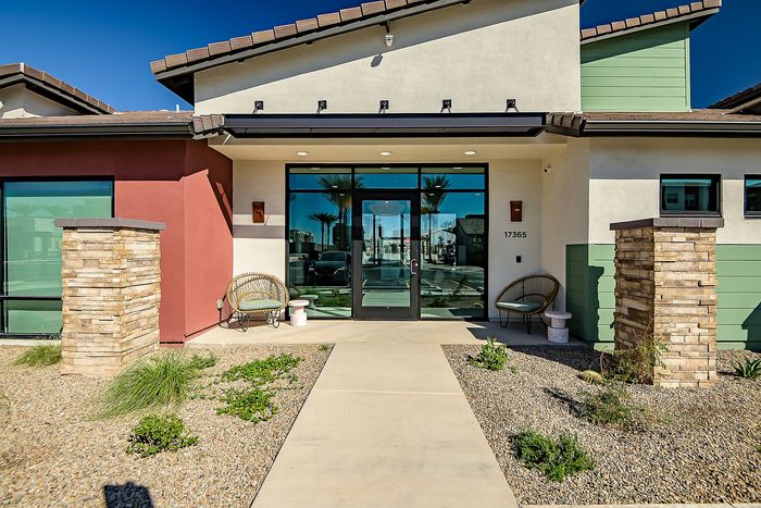 Modern entrance of an apartment building with stylish architectural design, featuring vibrant color contrast and cozy outdoor seating.