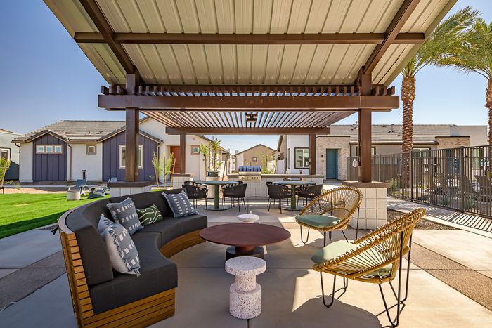 Modern outdoor seating area with stylish furniture beneath a pergola, surrounded by palm trees and contemporary homes.