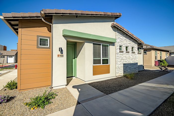 Charming modern home with a sleek design, featuring a textured facade and inviting entrance, set against a clear blue sky.