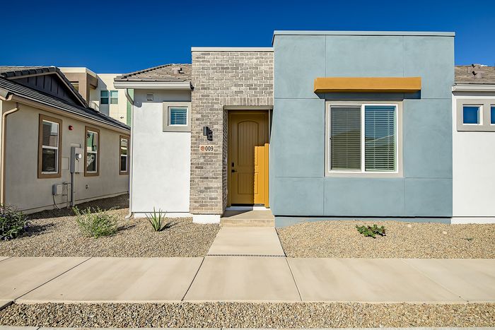 Charming modern home facade with stylish brick and blue exterior, featuring an inviting yellow door and neat landscaping.