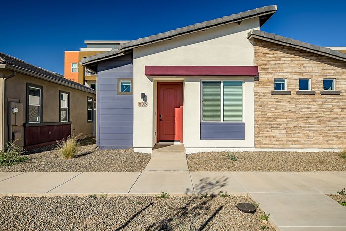 Charming modern house exterior featuring a vibrant red door, artistic stonework, and sleek blue paneling under a clear blue sky.