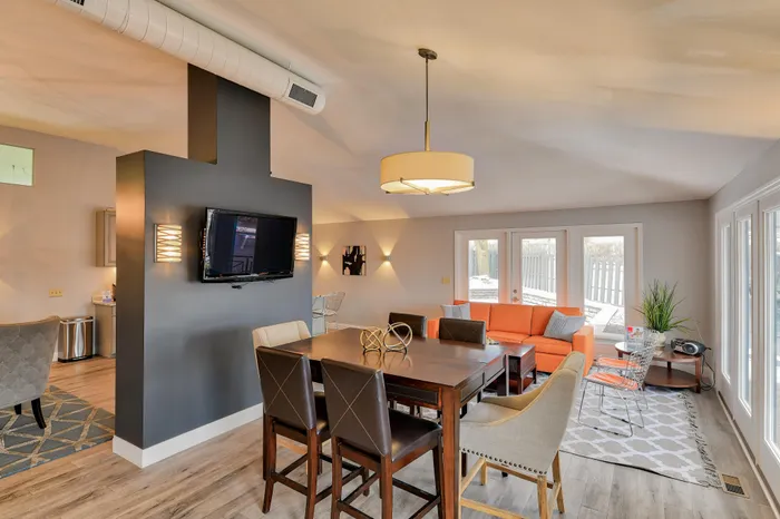Bright and inviting open-plan living area featuring a contemporary dining space, vibrant orange couch, and large windows offering ample natural light.