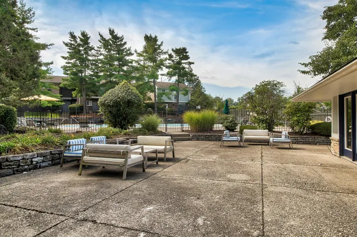 Inviting outdoor patio area with stylish seating, lush greenery, and a view of the swimming pool in a serene residential setting.