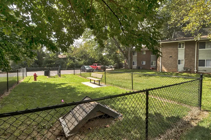 Charming apartment complex featuring a lush, fenced dog park with seating area and vibrant greenery.