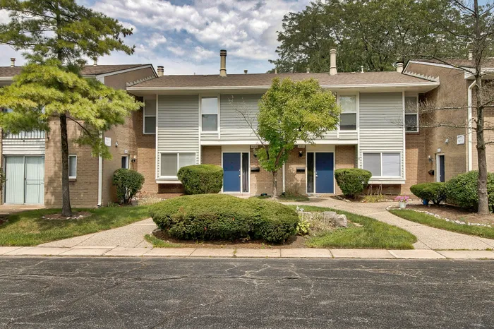 Charming townhouse exterior with brick facade, lush landscaping, and vibrant blue doors.