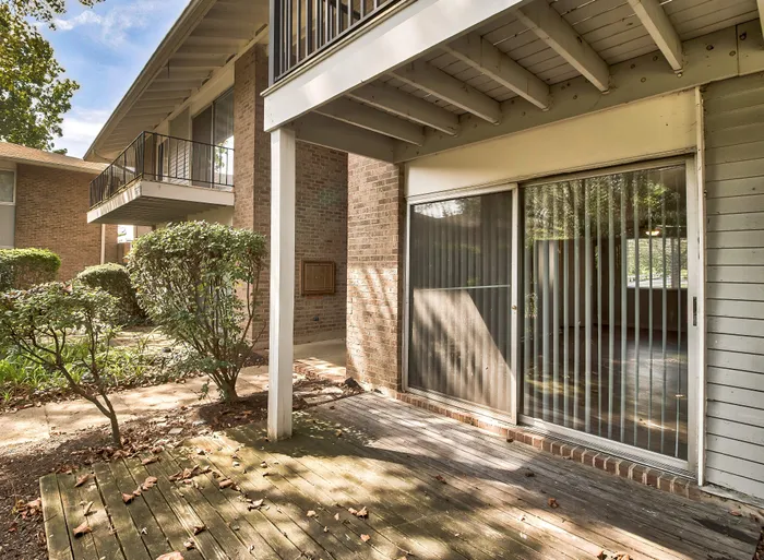 Charming apartment patio with sliding glass doors, surrounded by lush greenery and a cozy balcony above.