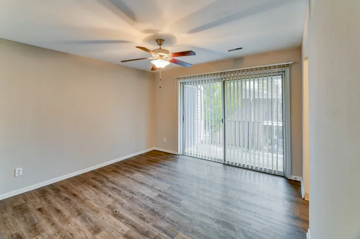 Elegant living room with rich wooden floors, ceiling fan, and floor-to-ceiling windows offering abundant natural light.